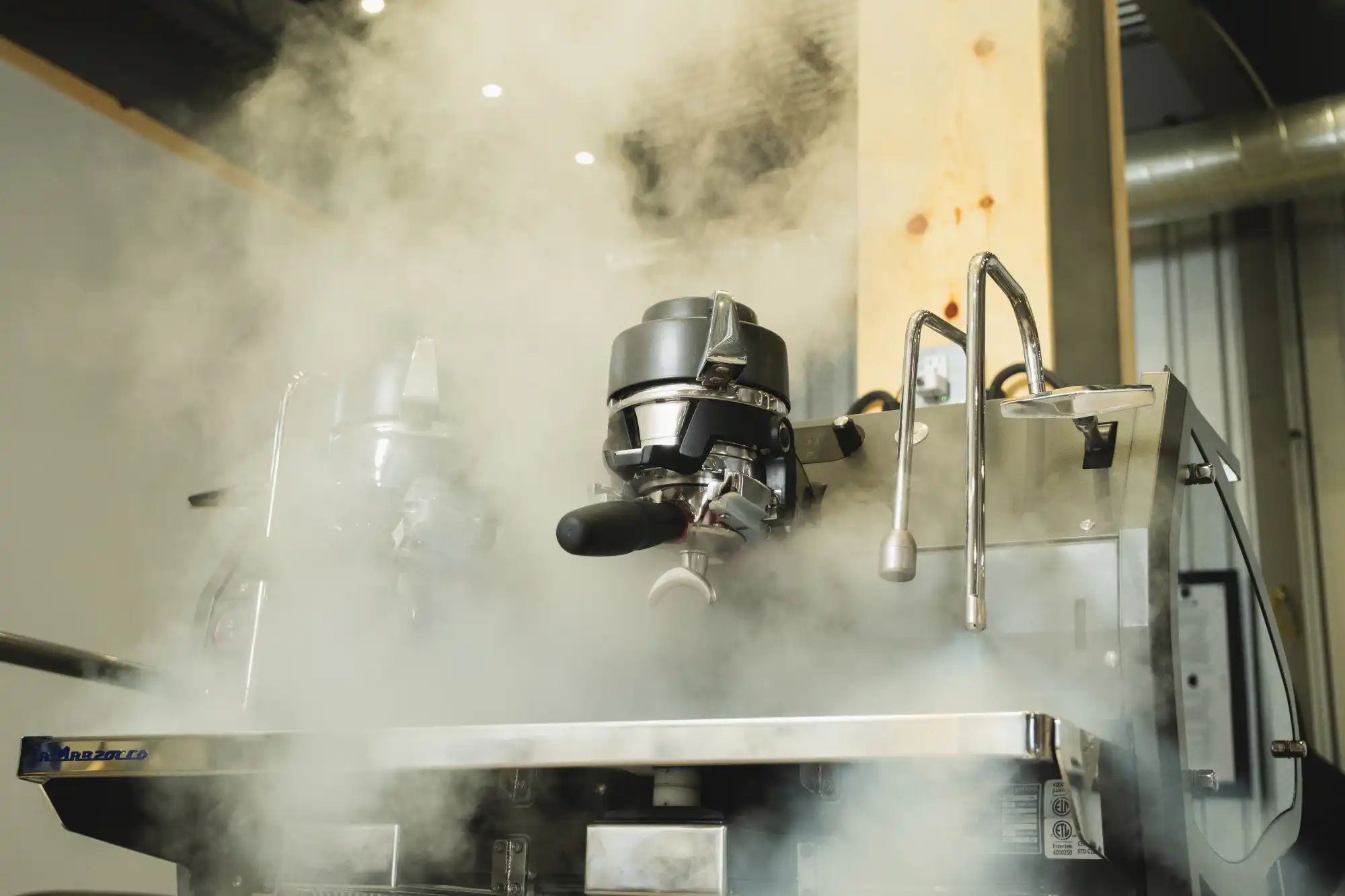 Steam rising around the group head of an espresso machine